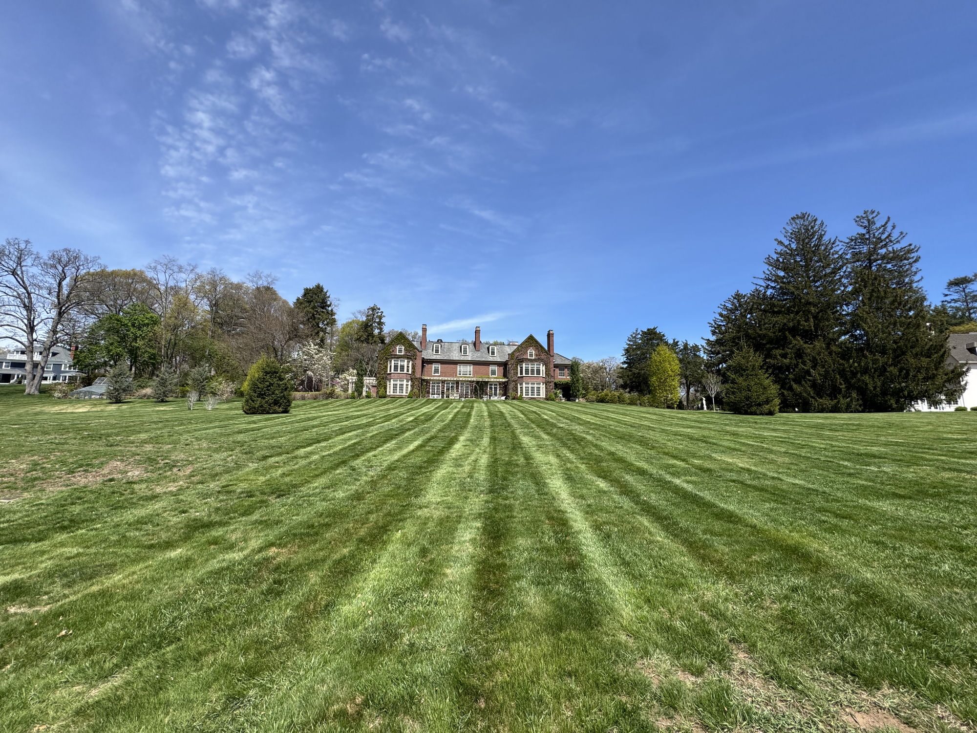 Wide front lawn with even mowing stripes leading to a large brick and stone manor home
