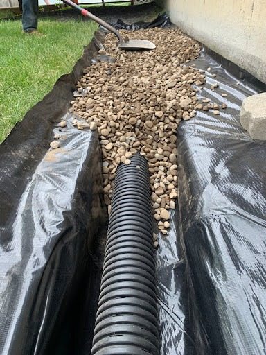 French drain trench lined with fabric and gravel during a drainage installation