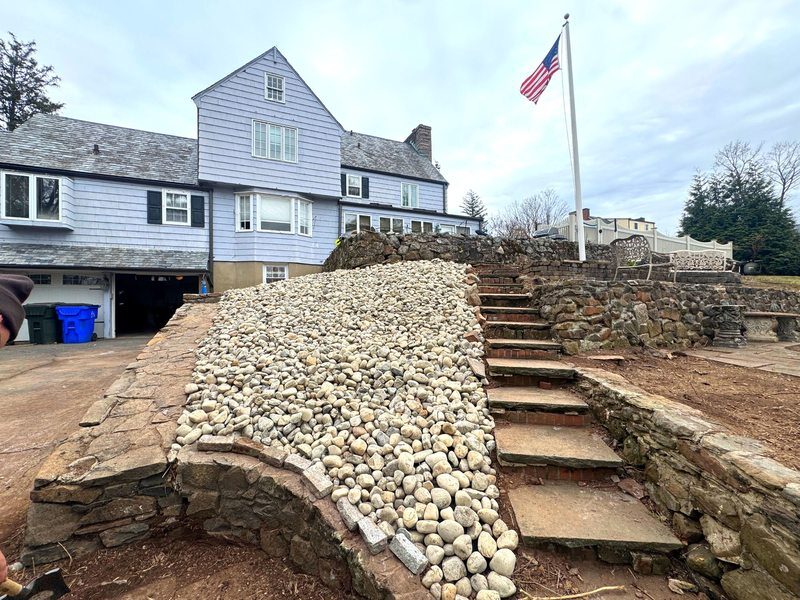 Stone steps and river-rock drainage border installed at a residential entrance